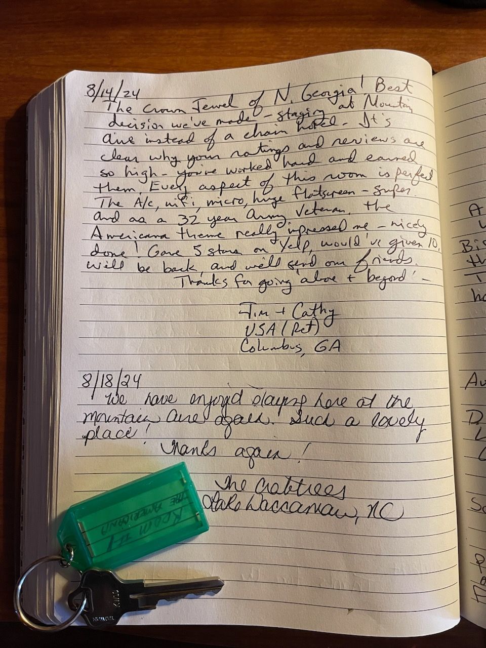 Open notebook with handwritten entries, a green key tag, and a key, on a wooden surface.