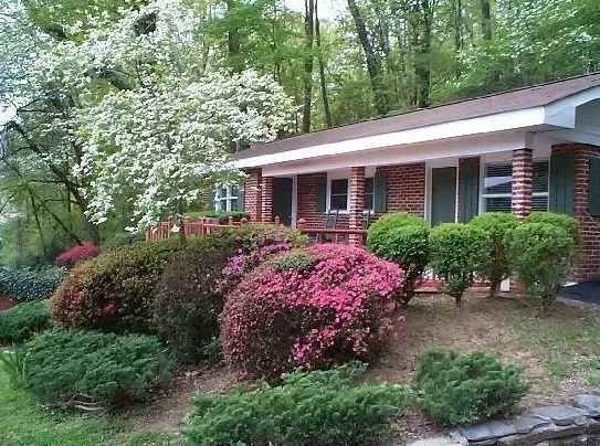 Brick house with colorful azalea bushes in front. White flowering tree to the left.