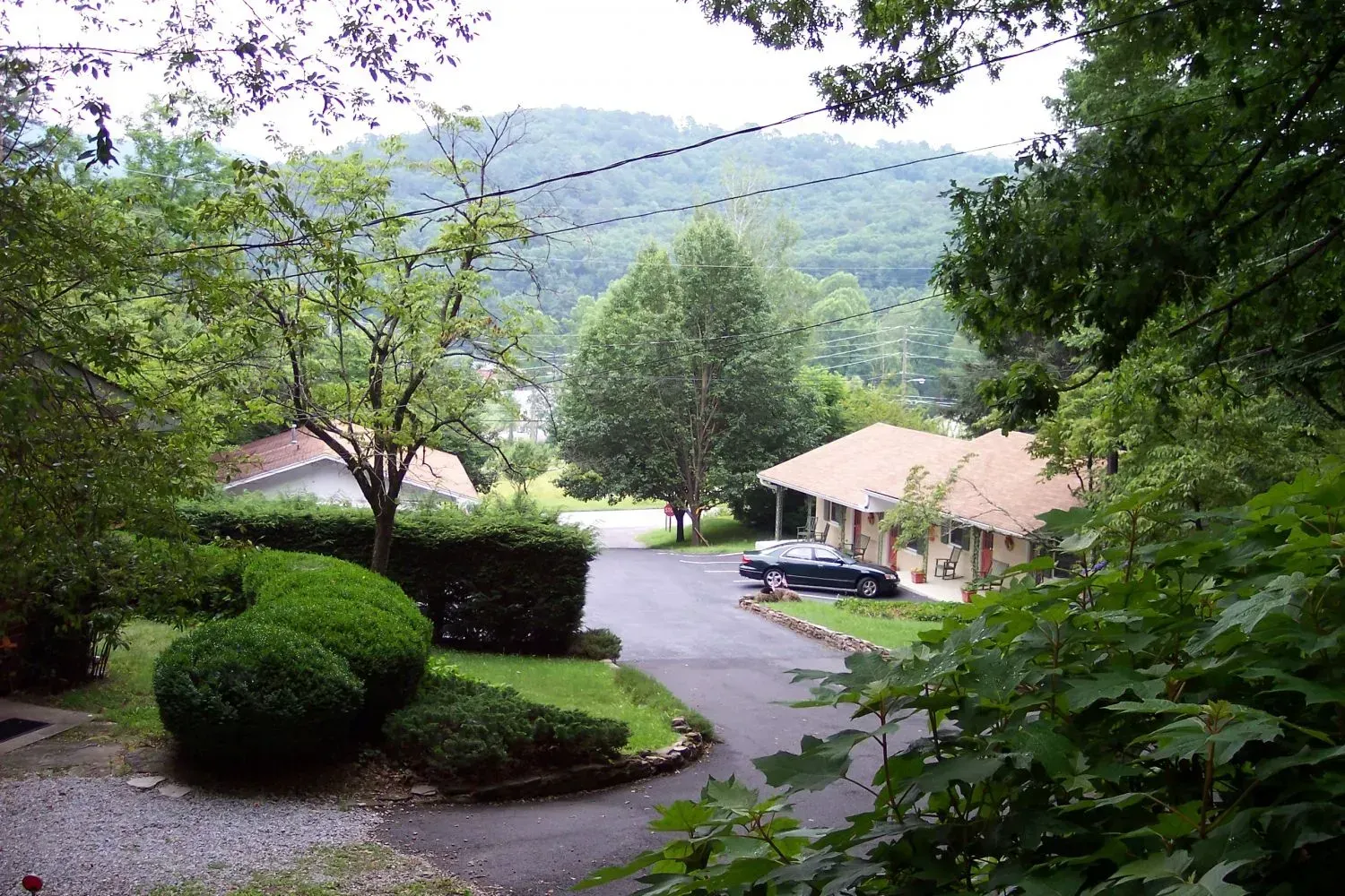 Road leading to motel nestled in a valley with trees and a mountain in the background.