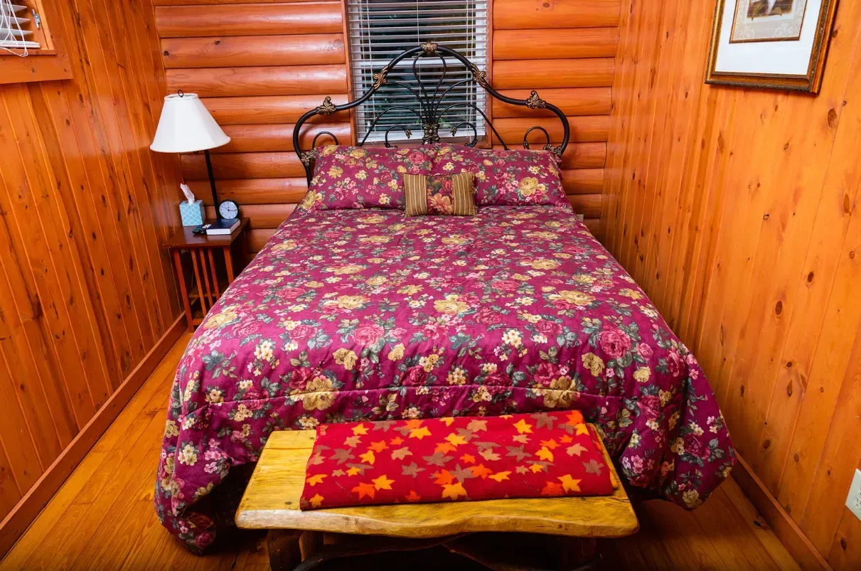 Cozy cabin bedroom with a maroon floral bedspread, wooden walls, and a rustic bench.