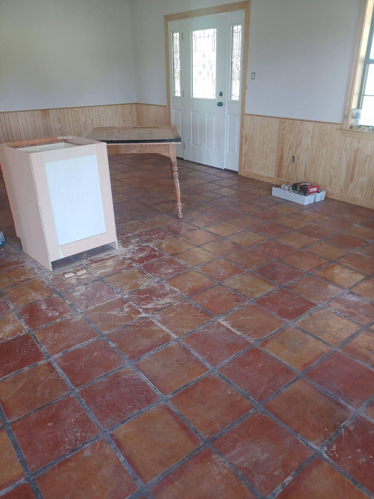 Room with reddish-brown tile floor, unfinished walls, and cabinet; door and table visible.