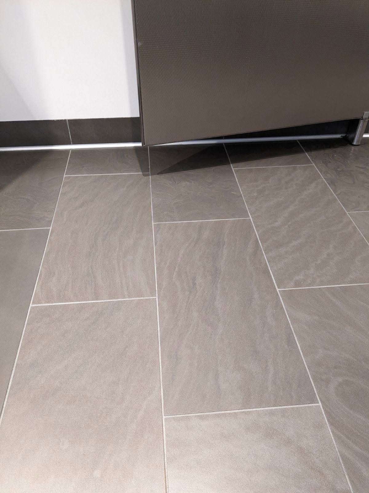 Gray tiled floor with grout lines, a dark gray wall edge, and a white wall corner.