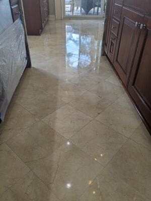Beige tile floor in a kitchen, reflecting sunlight. Wooden cabinets on the right, a covered object on the left.