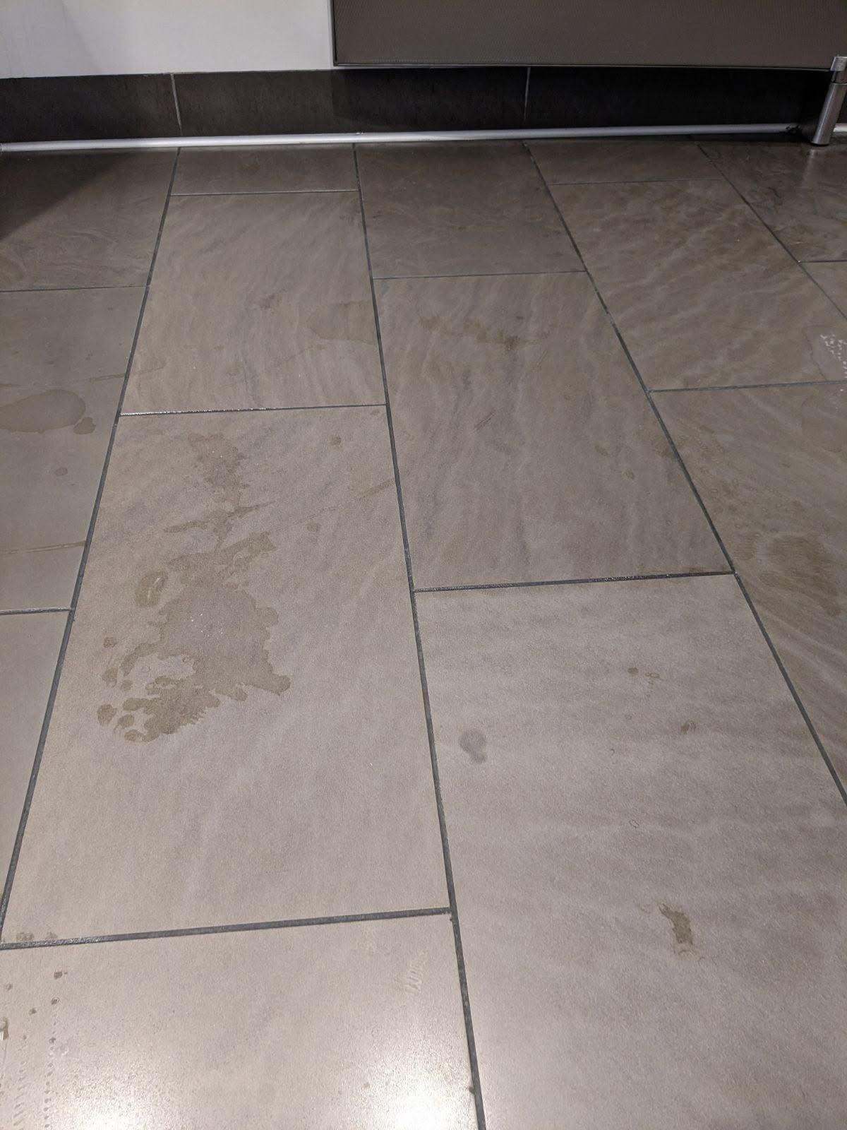 Gray tile floor with water stains near a white wall.