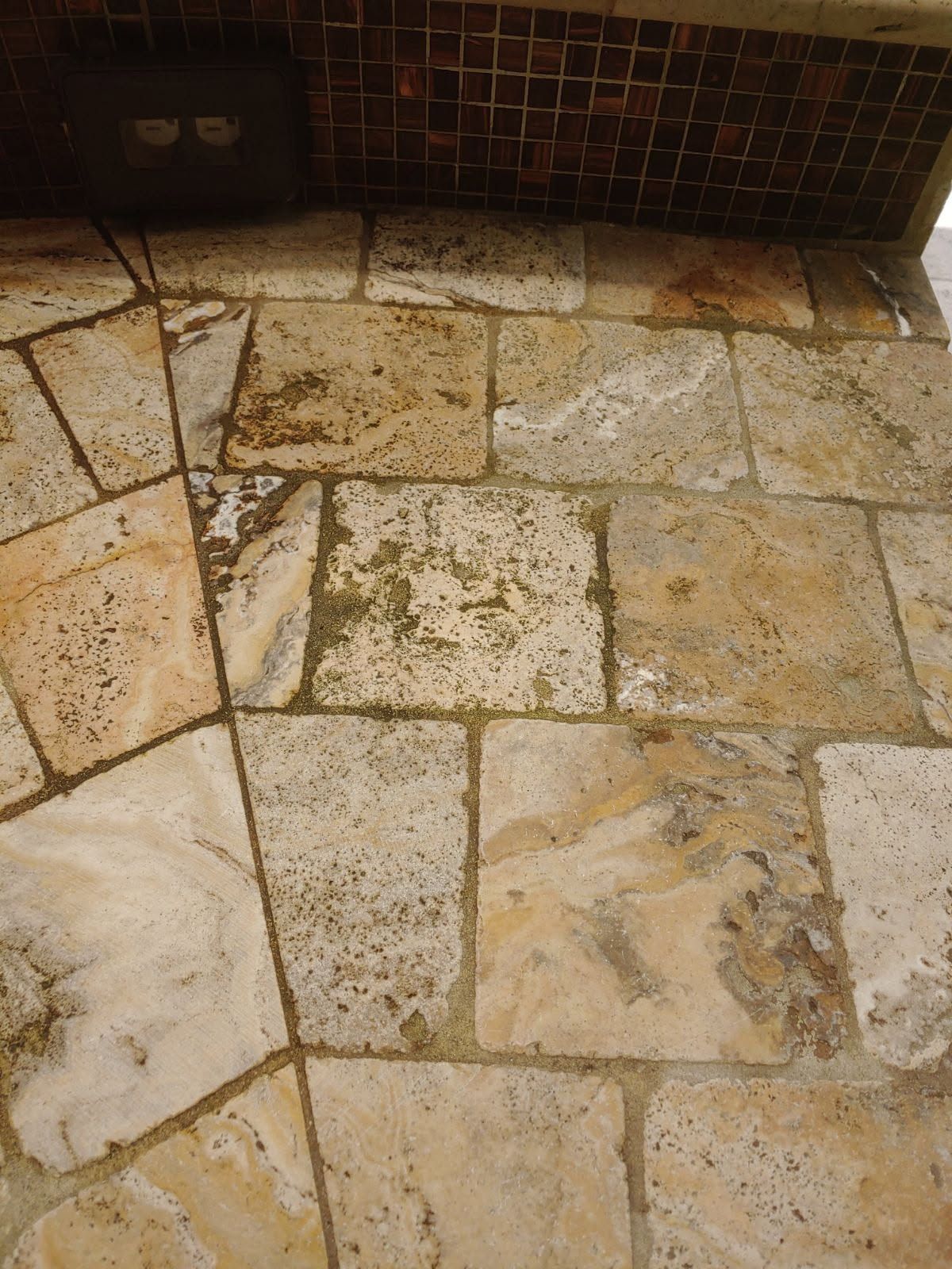 Beige stone floor with grout, under a dark, tiled structure.