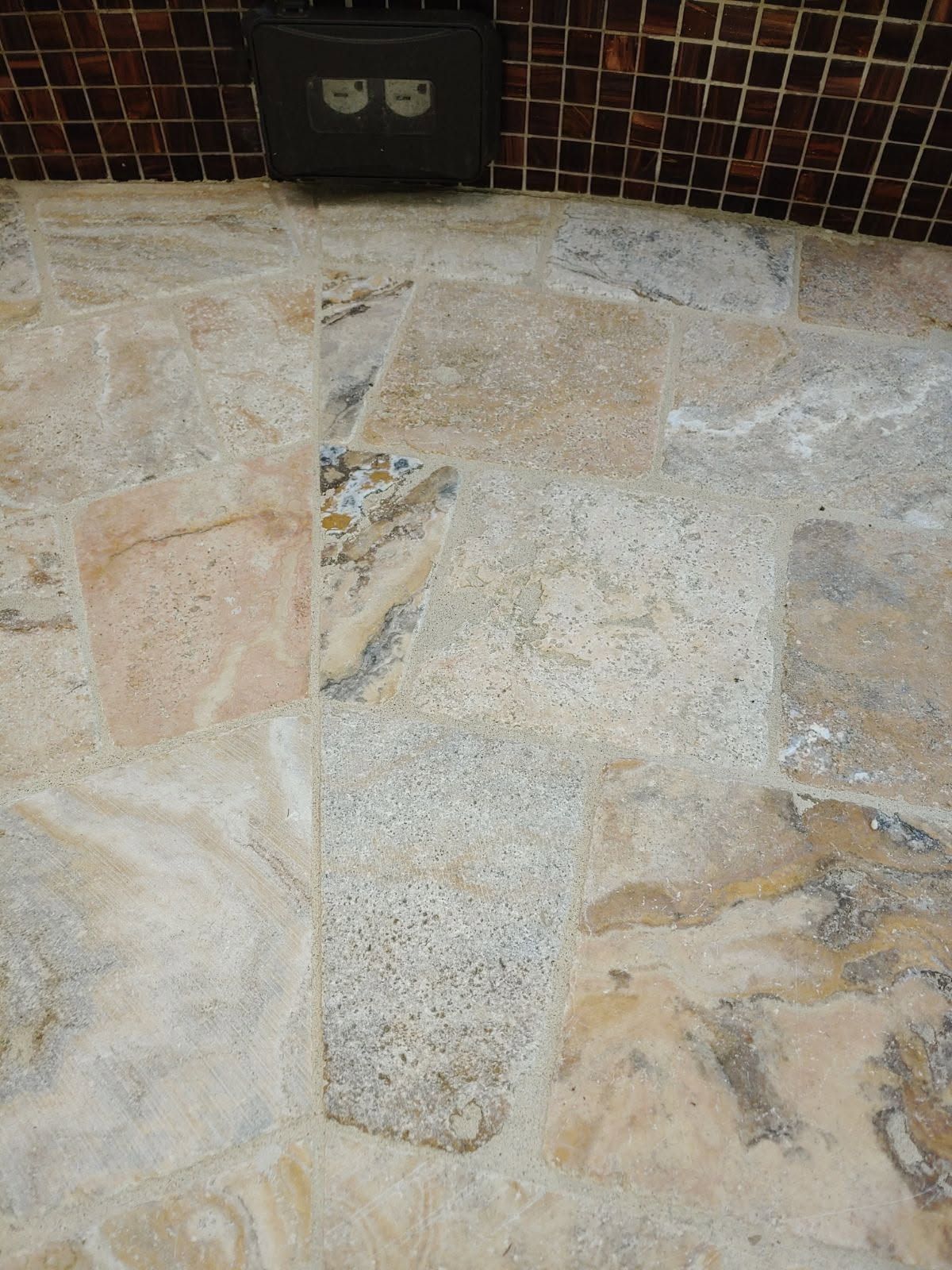 Tiled floor with varying shades of beige, tan, and gray; a dark outlet box is above.
