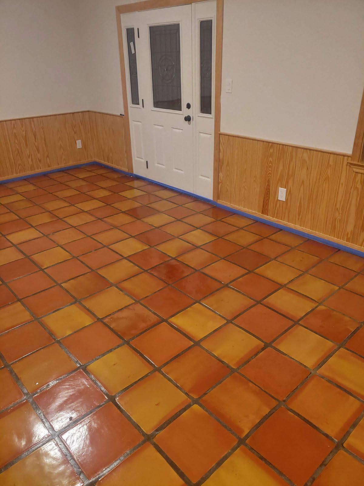 Orange and yellow tile floor in a room with white door, light wood paneling, and beige walls.