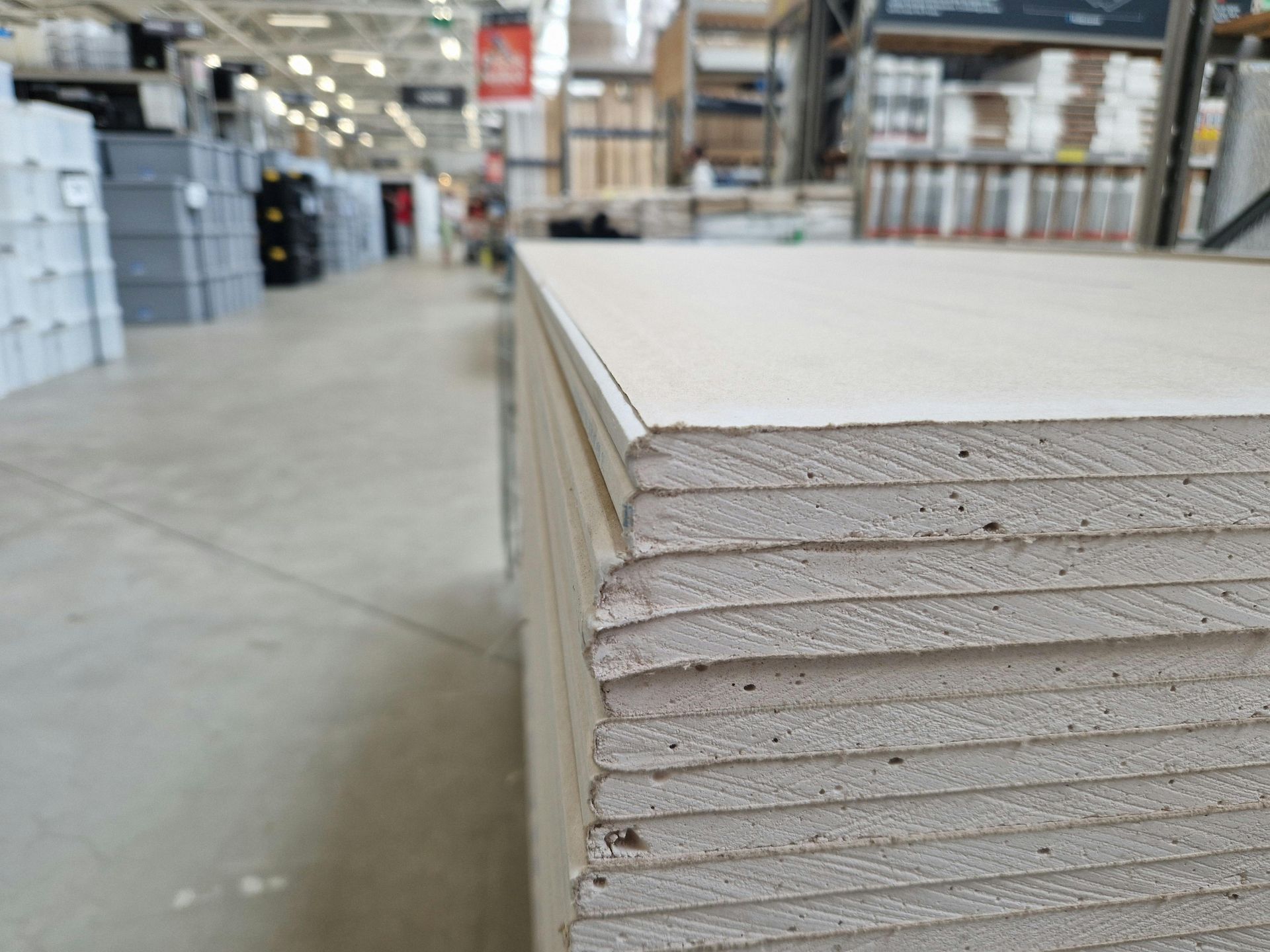Stack of drywall sheets in a hardware store aisle, with a blurred background.