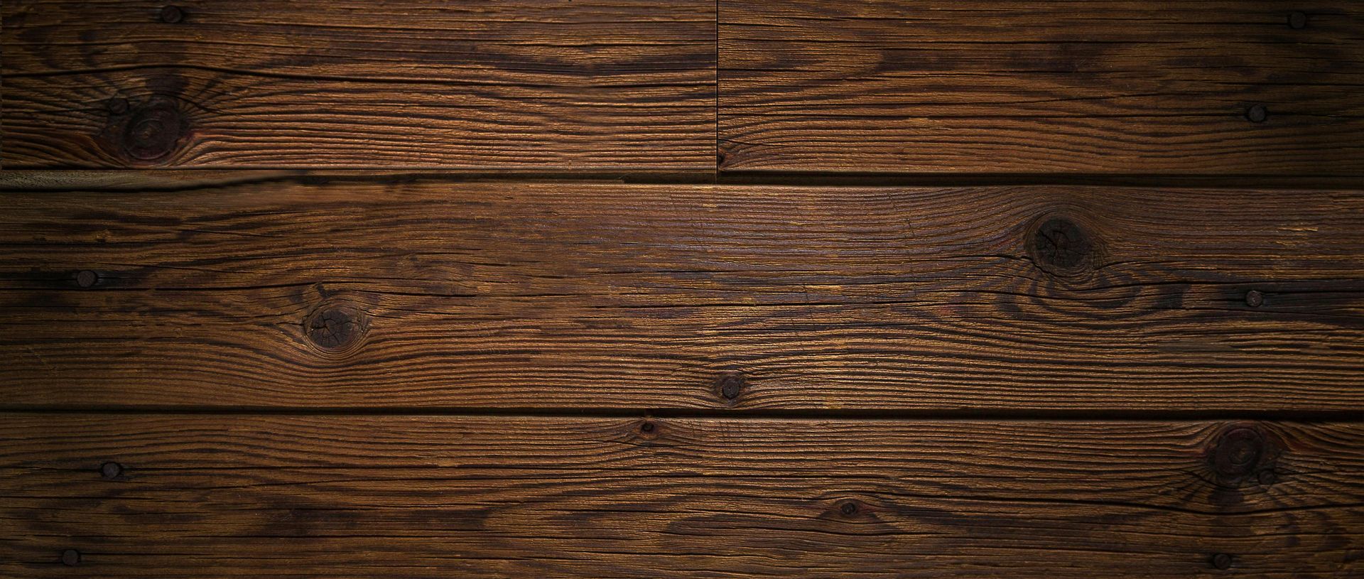 Close-up of weathered, dark brown wooden planks, with visible knots and grain.