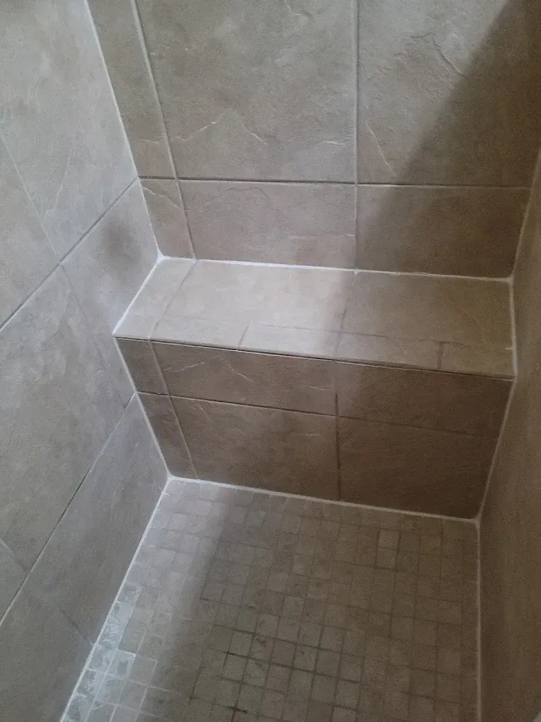 Shower stall with built-in tiled bench; beige tiles; wet floor with small tiles.