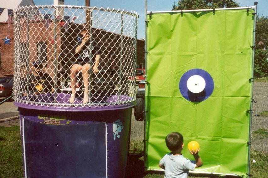 A little boy is throwing a ball at a target in a dunk tank