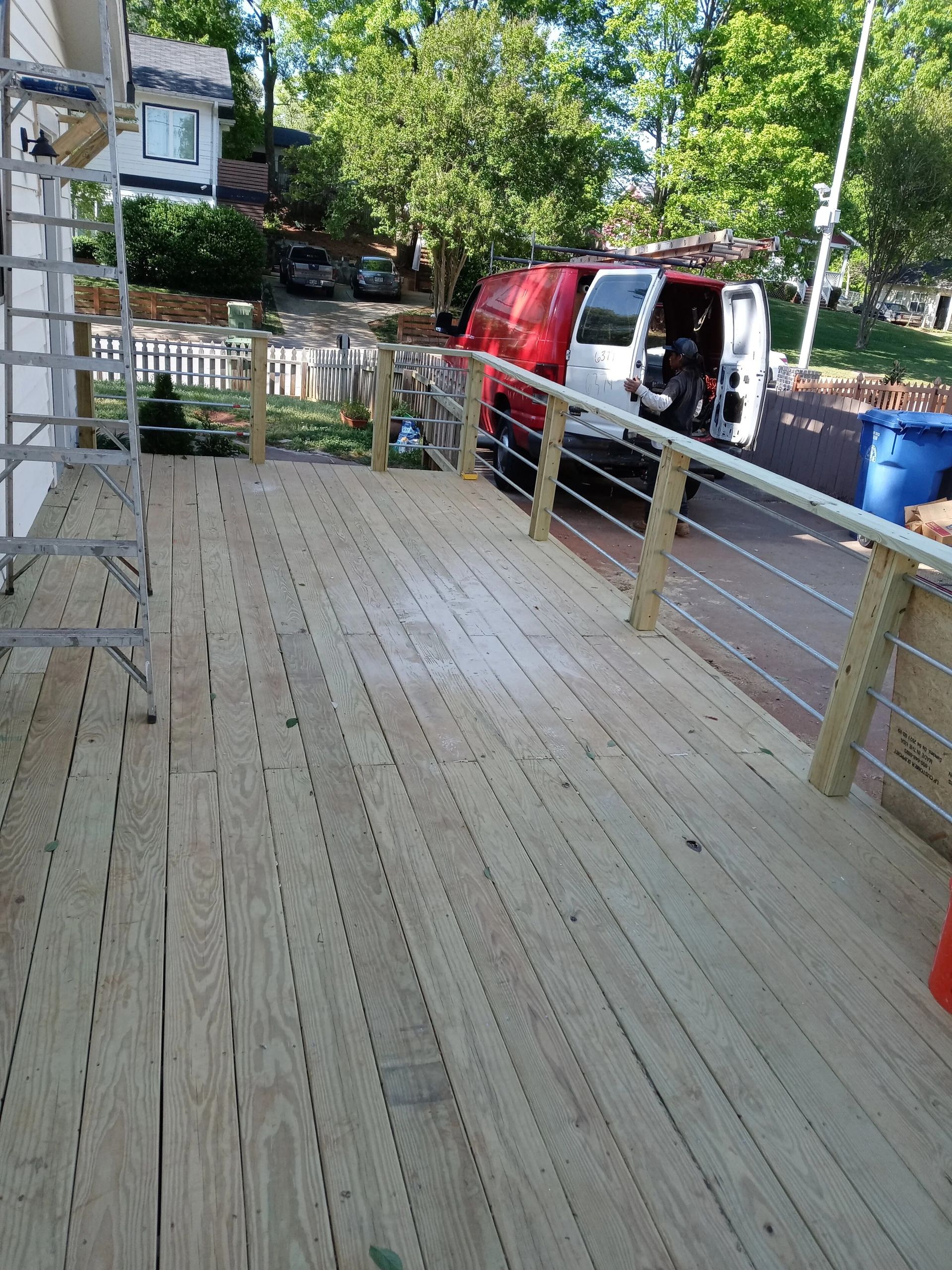 Wooden deck with metal railing; red and white van parked in background.