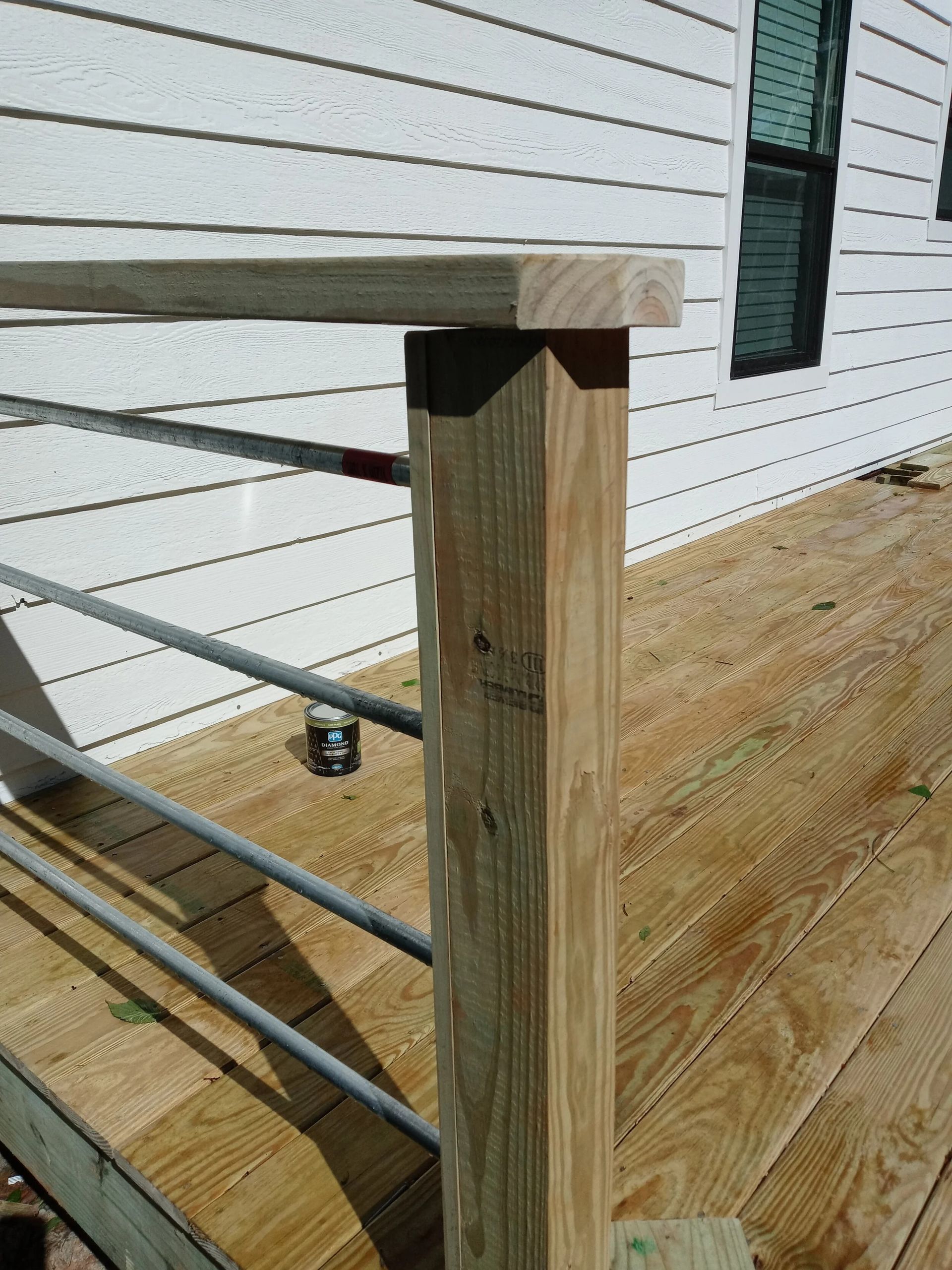 Wooden deck railing under construction, with square post, top rail, and horizontal metal bars.