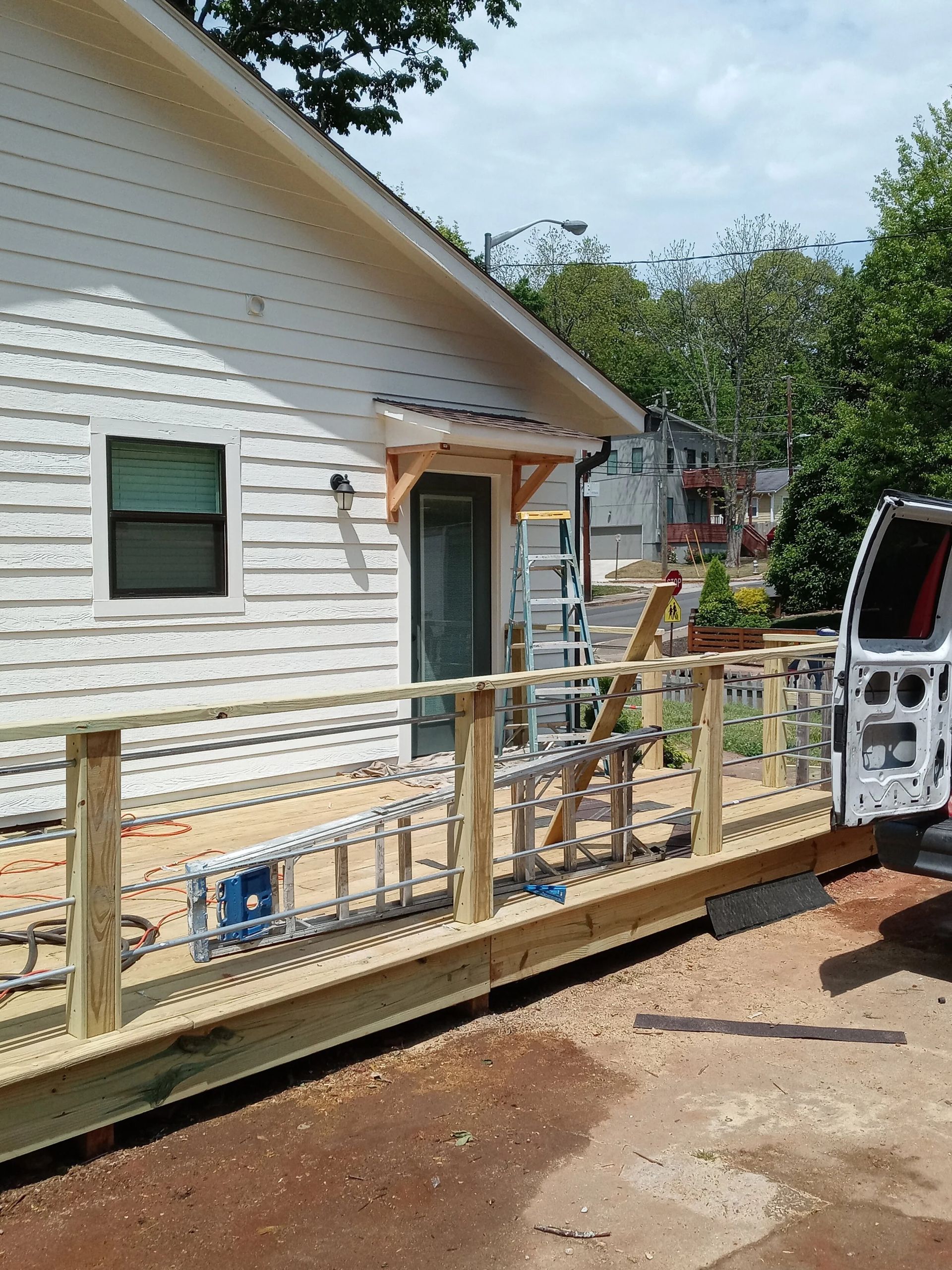 Newly built wooden deck with railing attached to a white building; construction tools nearby.