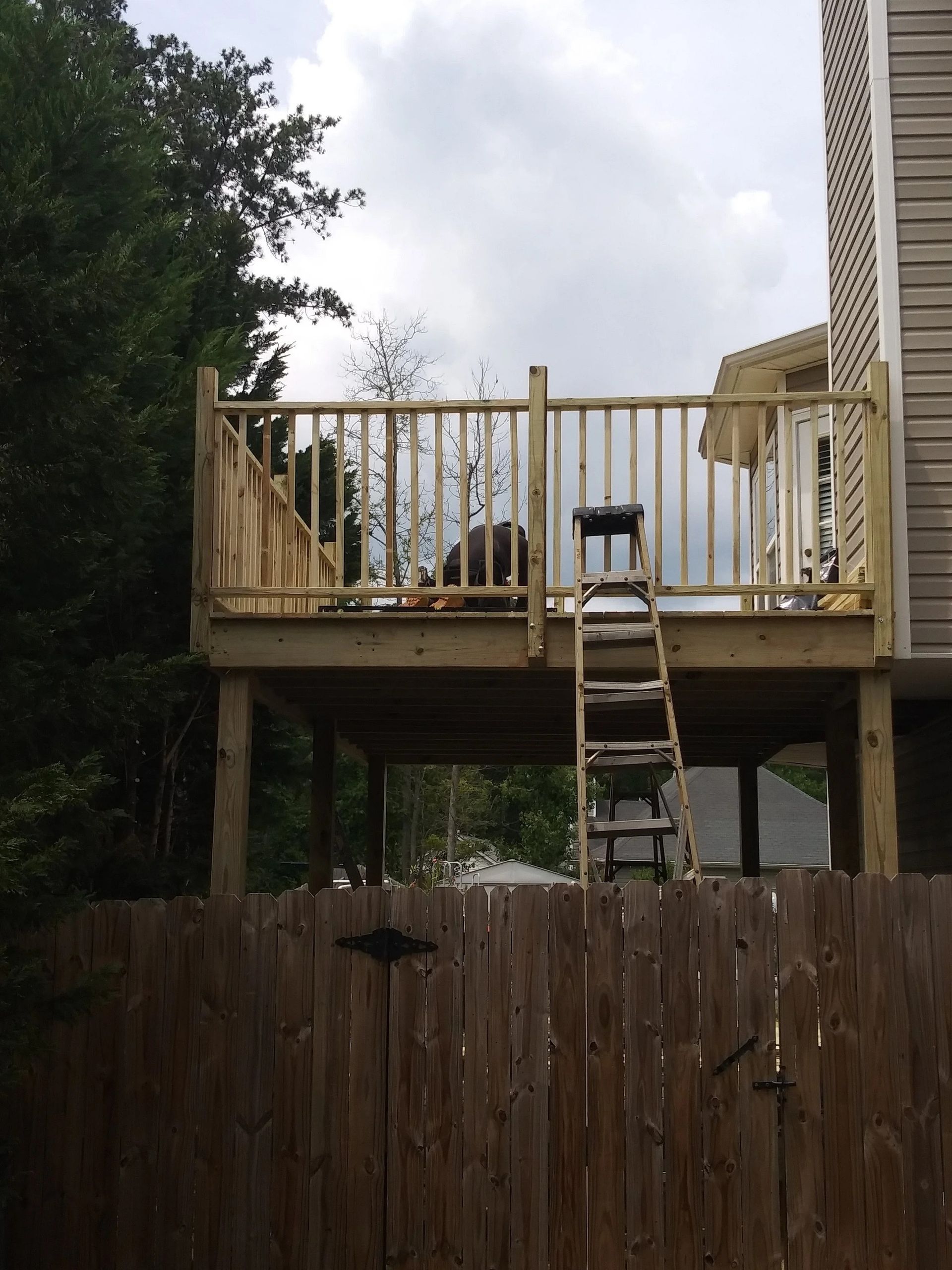 Wooden deck under construction with a ladder, against a cloudy sky.