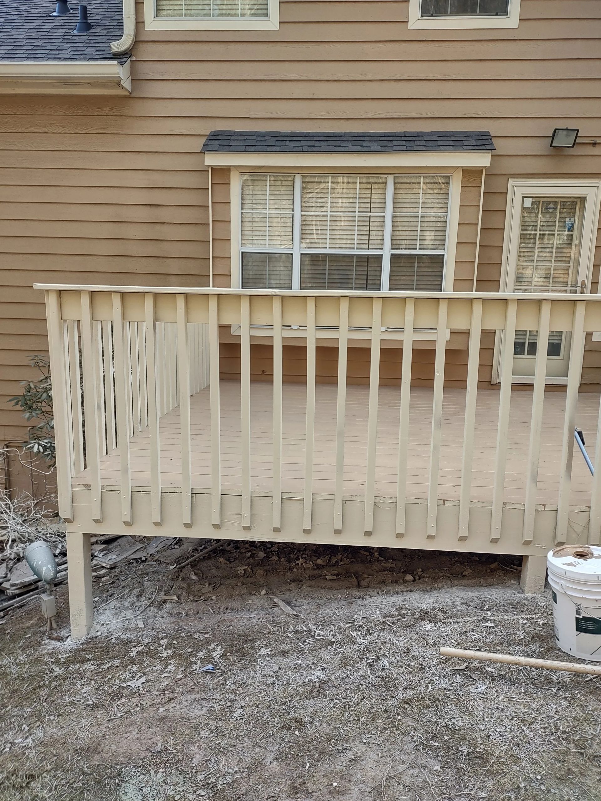 Tan deck with a white railing, in front of a tan house with a window.