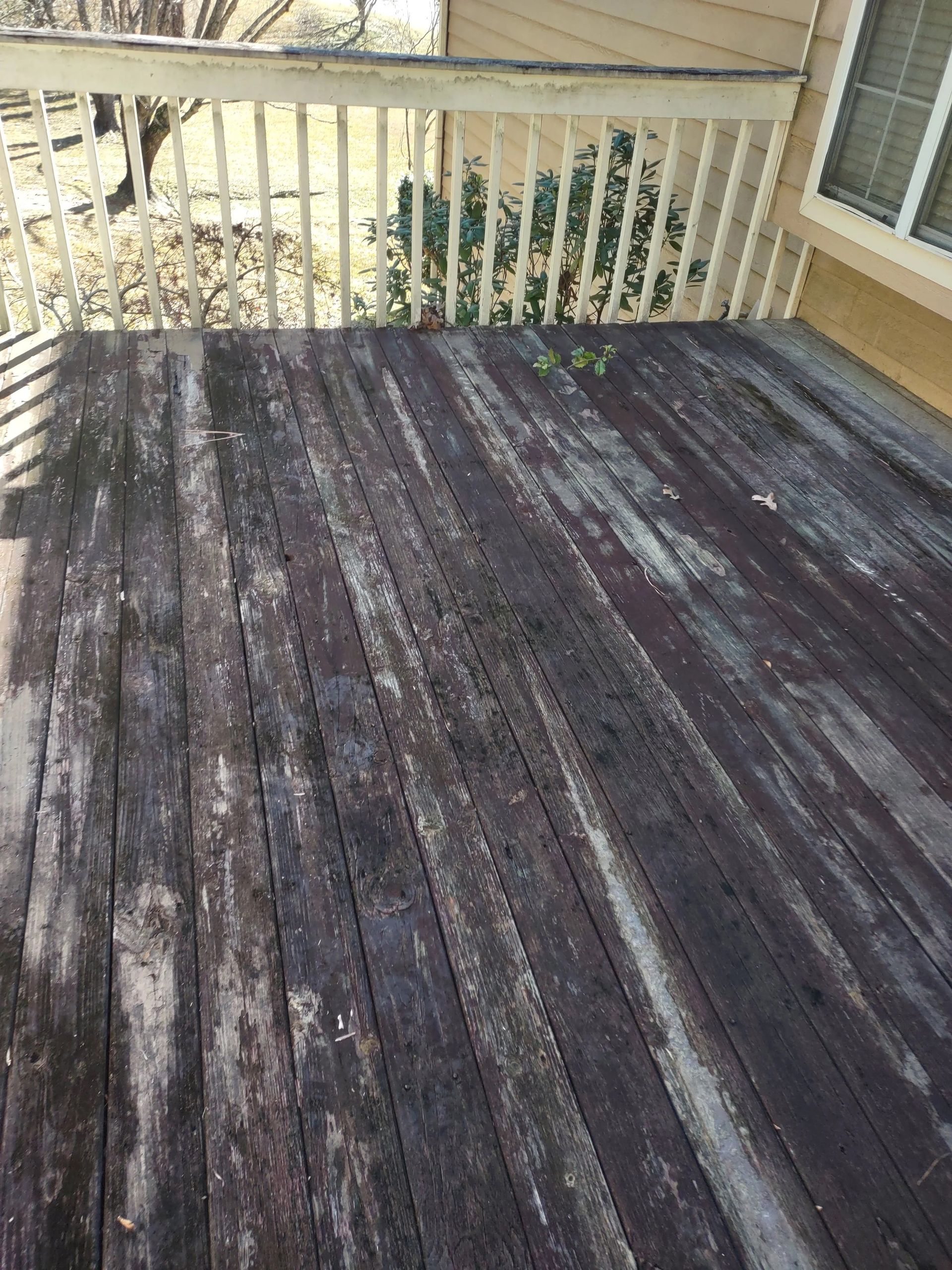Wooden deck with weathered, dark boards and light railing.