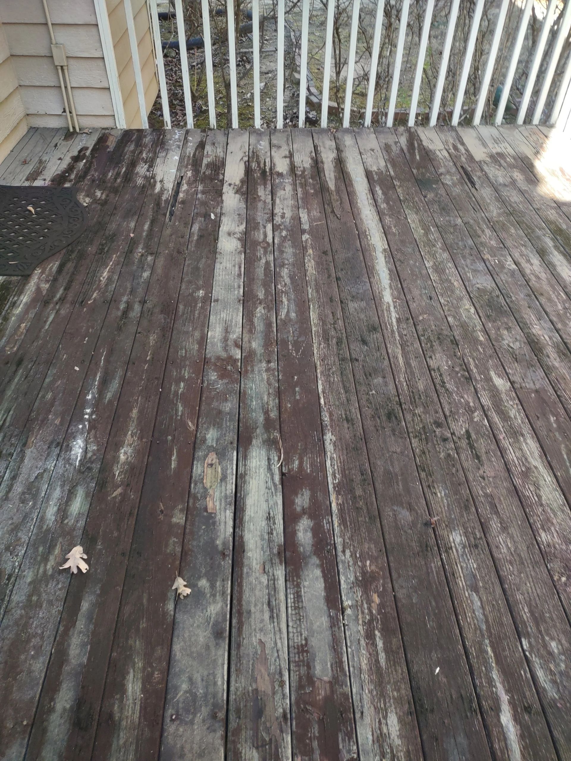 Wooden deck with worn, weathered boards; white railing in background.