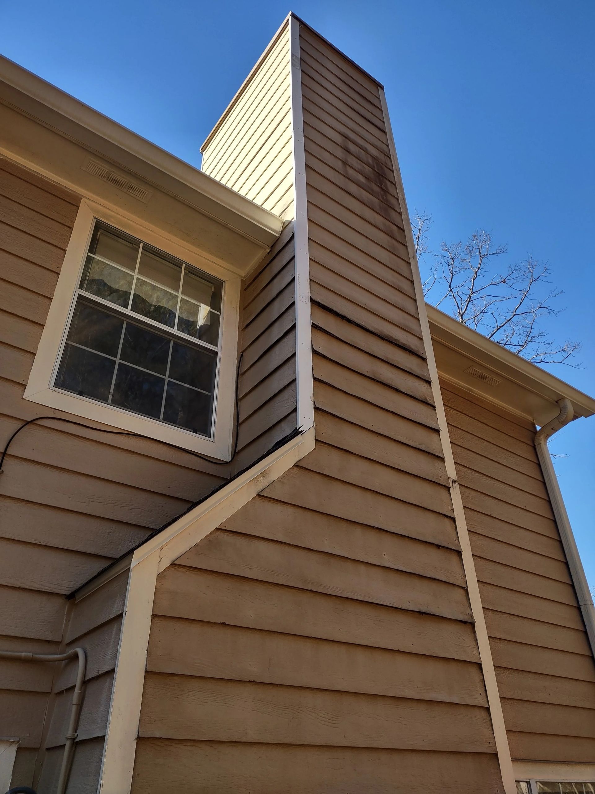 Exterior of a house with a brown chimney stained with soot. Blue sky backdrop.