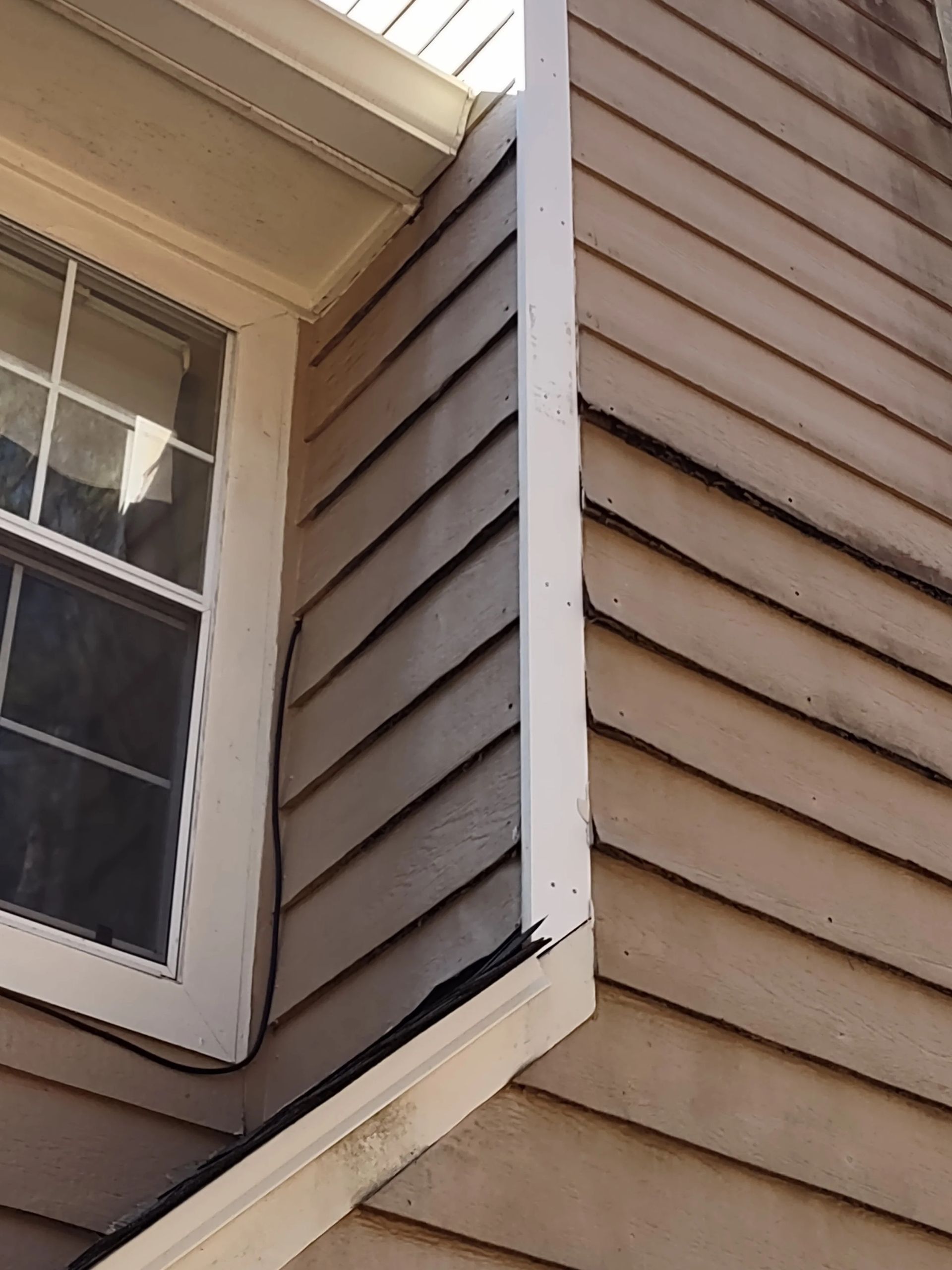 Corner of a house with weathered siding, white trim, and a window.