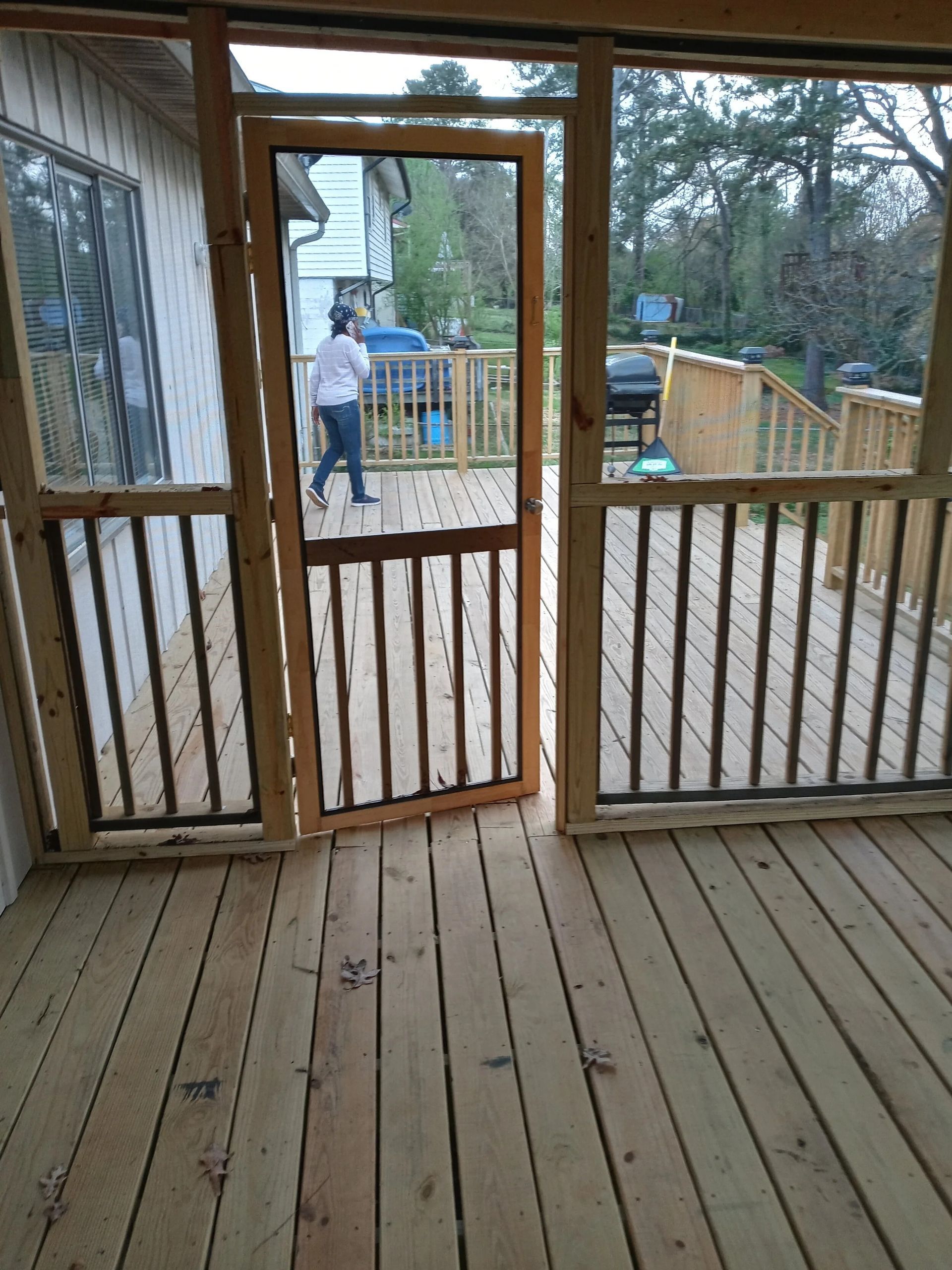 Wooden deck with screen door and railing. A person walks through the open door.