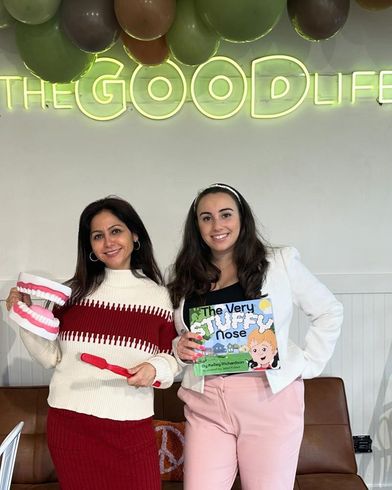 Two women are standing next to each other in front of a neon sign that says the good life.