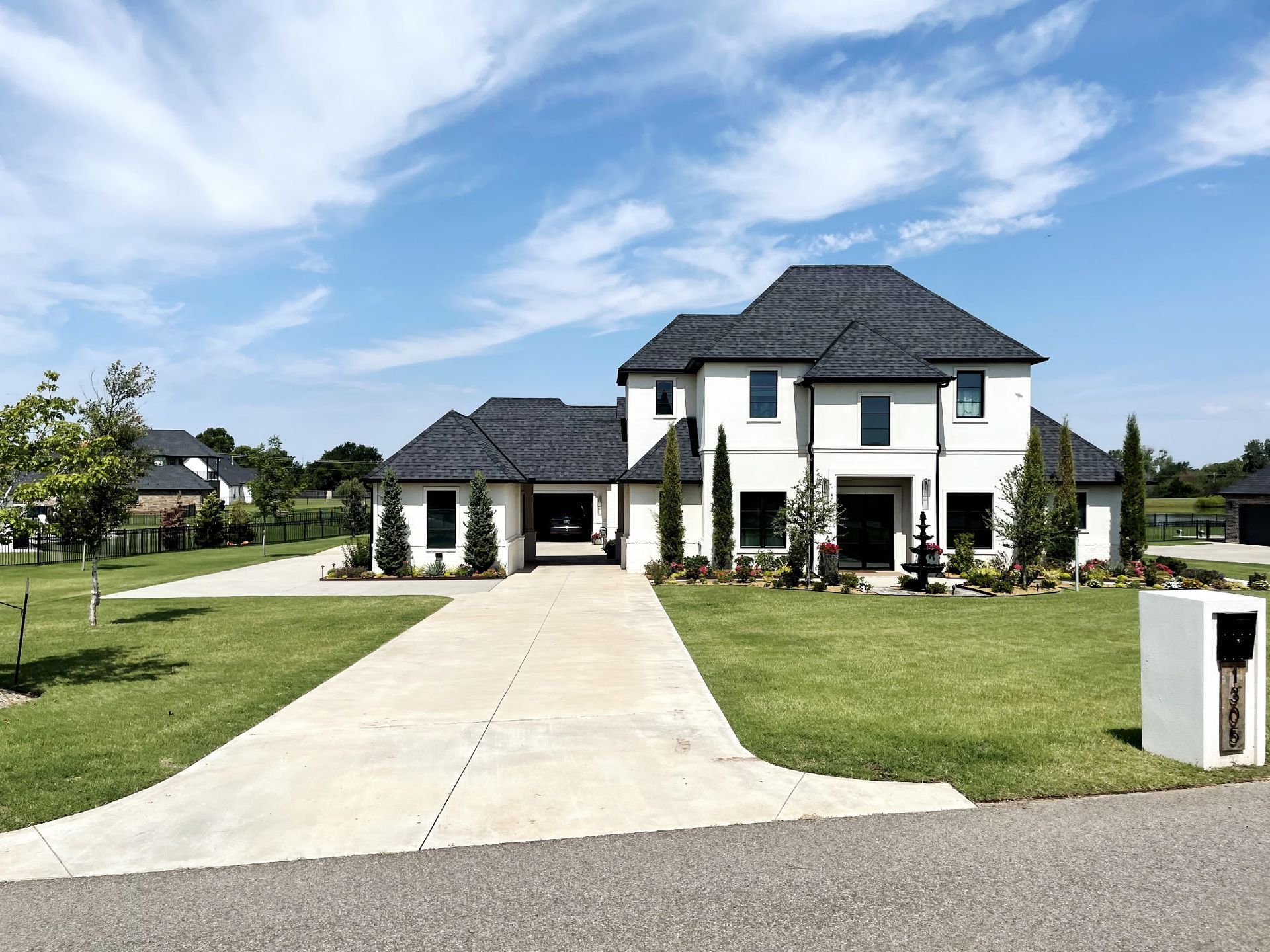Elegant white house with black roof, driveway, and lush green lawn under a blue sky.