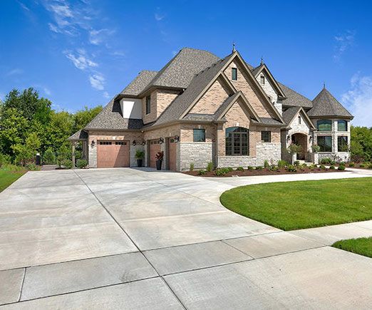 Large two-story house with brick and stone facade, attached garage, and a wide concrete driveway.
