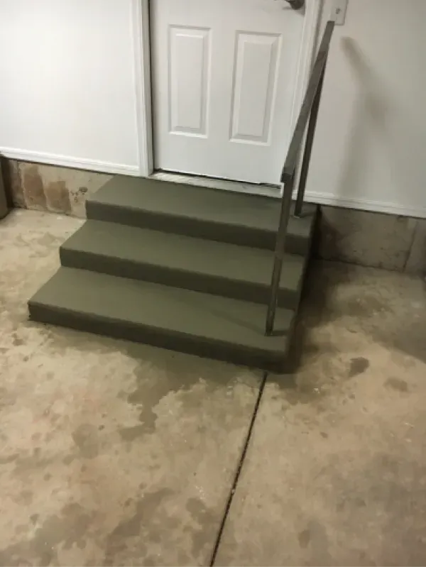 Concrete steps leading to a door with a metal handrail, in a garage.