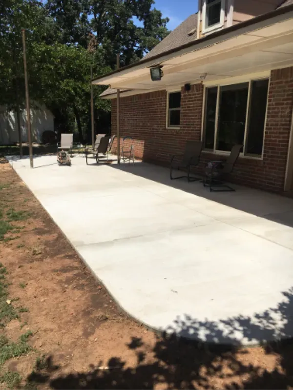 A newly poured concrete patio extends from a brick house with outdoor seating.