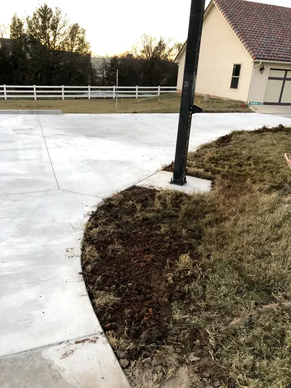 Concrete driveway, brown grass, and a house with a white fence. A utility pole is in the center.