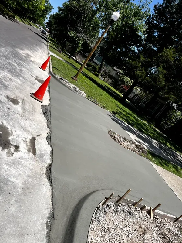 Freshly poured concrete curb next to a street, with orange traffic cones.
