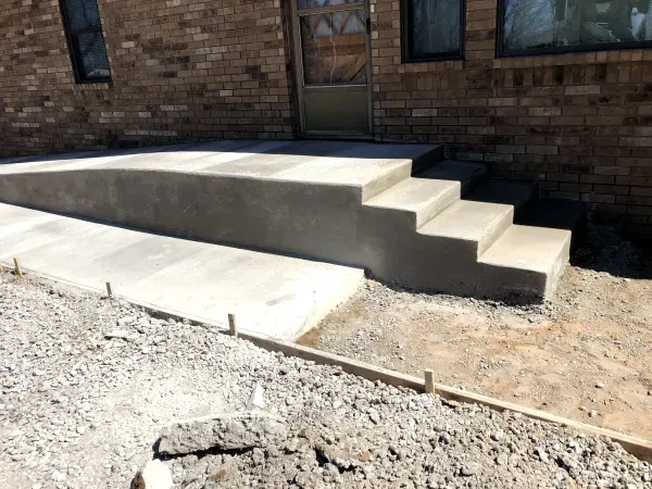 Concrete ramp and steps leading to a brick building's entrance, with gravel in the foreground.