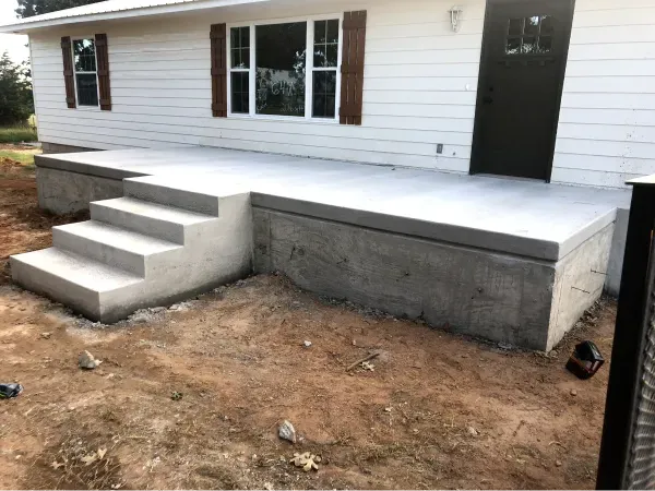 Gray concrete steps leading up to a door, next to a white house, construction materials on the ground.