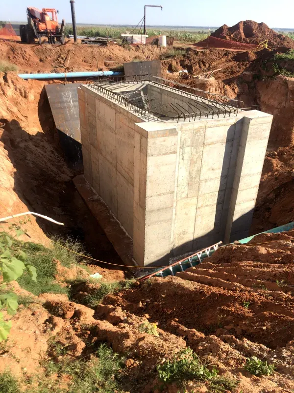 Concrete structure under construction in a deep ditch, with exposed rebar and blue pipes.
