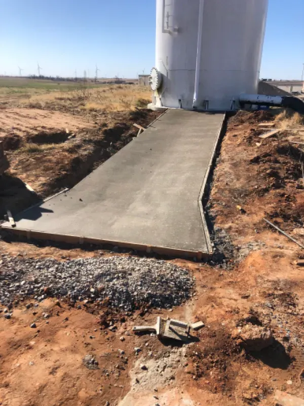 Newly poured concrete ramp leading to a large white cylindrical structure on a construction site.