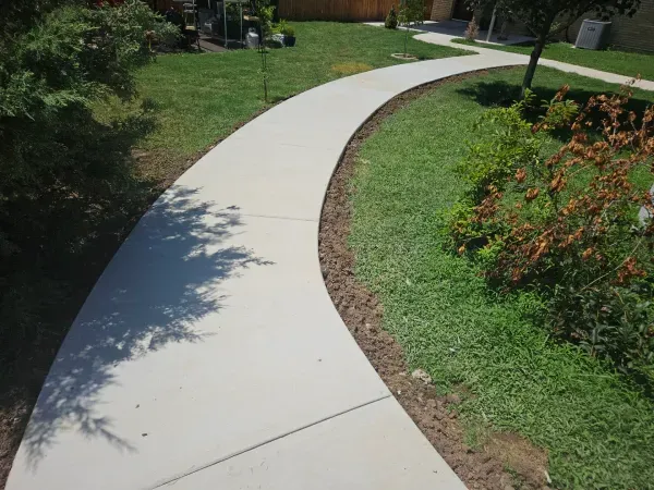 Concrete walkway curves through a green grassy yard.
