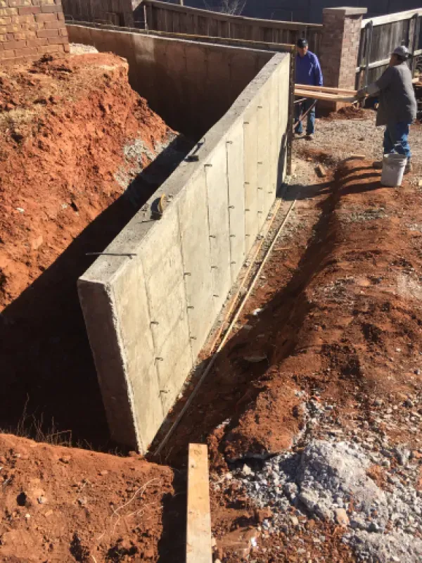 Concrete foundation wall under construction, workers nearby. Earth-toned setting.