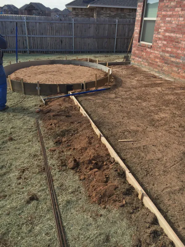 Construction site with wooden forms outlining a circular area and a walkway, set in a yard.