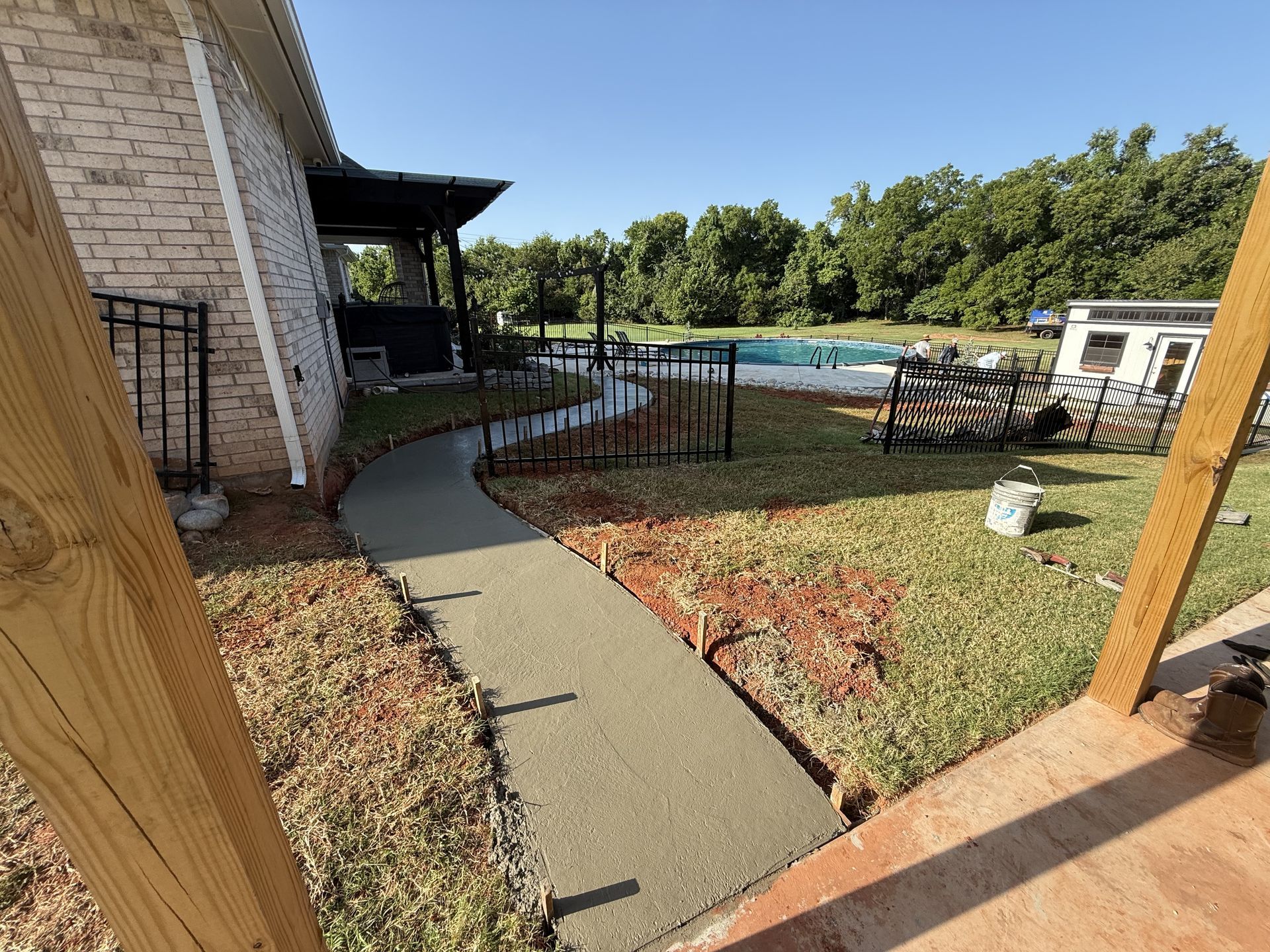 New concrete walkway curves through yard towards a swimming pool.