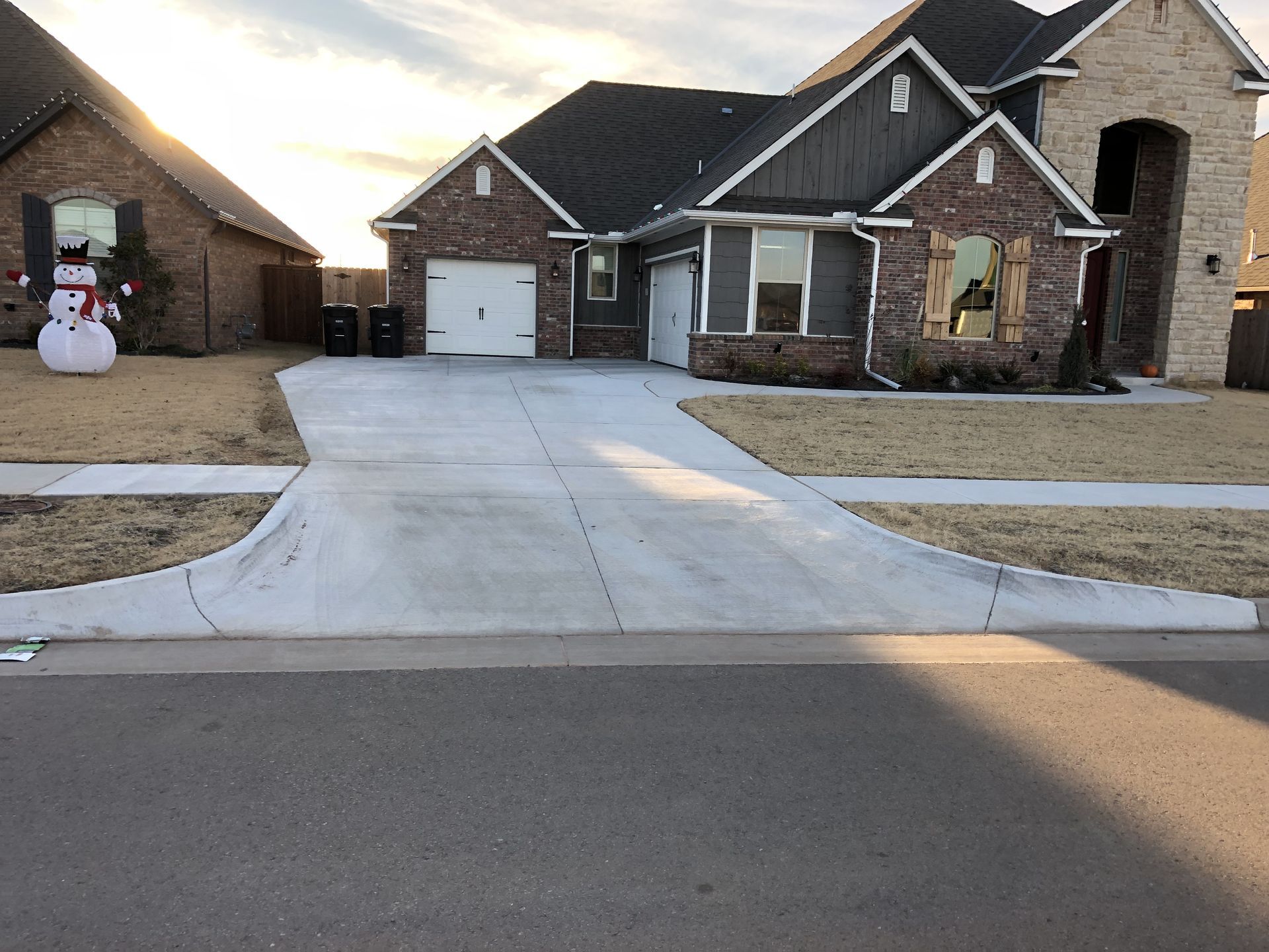 A house with a gray driveway and brick facade, with a snowman decoration in the yard.