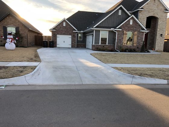 A house with a gray driveway and brick facade, with a snowman decoration in the yard.