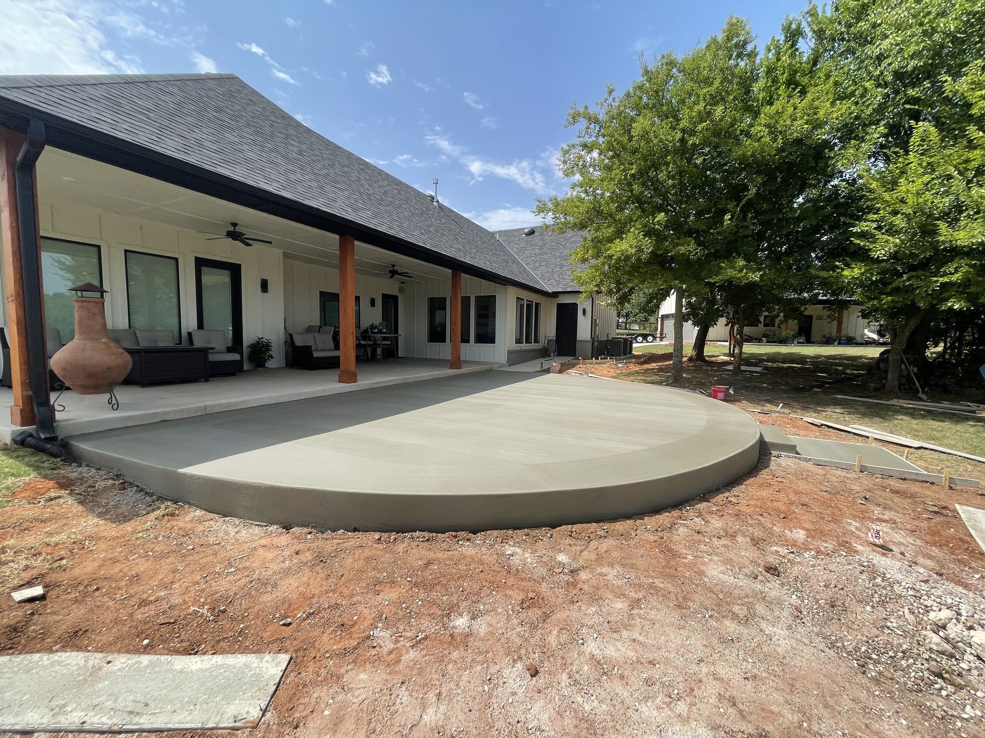 Newly poured concrete patio extending from a white house with a black roof.