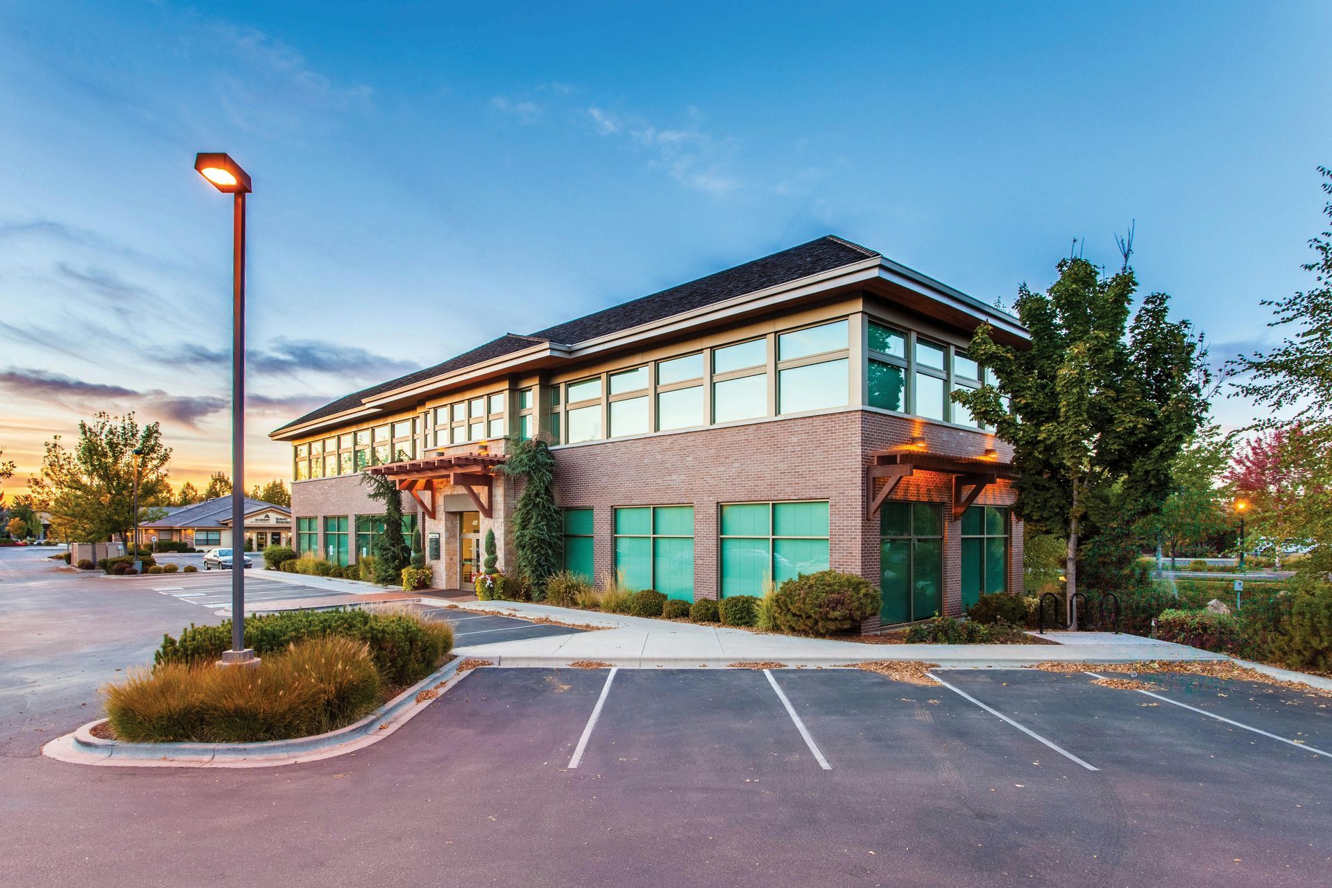 Office building with parking lot; brown brick facade, large windows, blue sky.