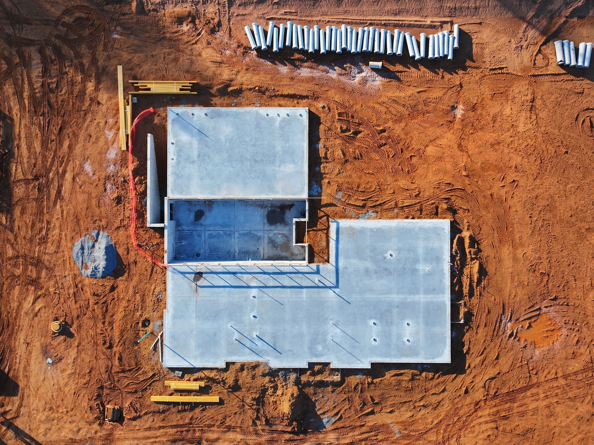 Overhead view of a concrete foundation with exposed rebar on a construction site, surrounded by dirt and building materials.