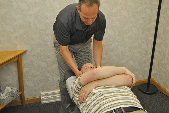 A Woman Is Sitting On A Bed While A Doctor Examines Her Back - Findlay, OH - Blanchard Valley Chiropractic A Woman Is Sitting On A Bed While A Doctor Examines Her Back - Findlay, OH - Blanchard Valley Chiropractic