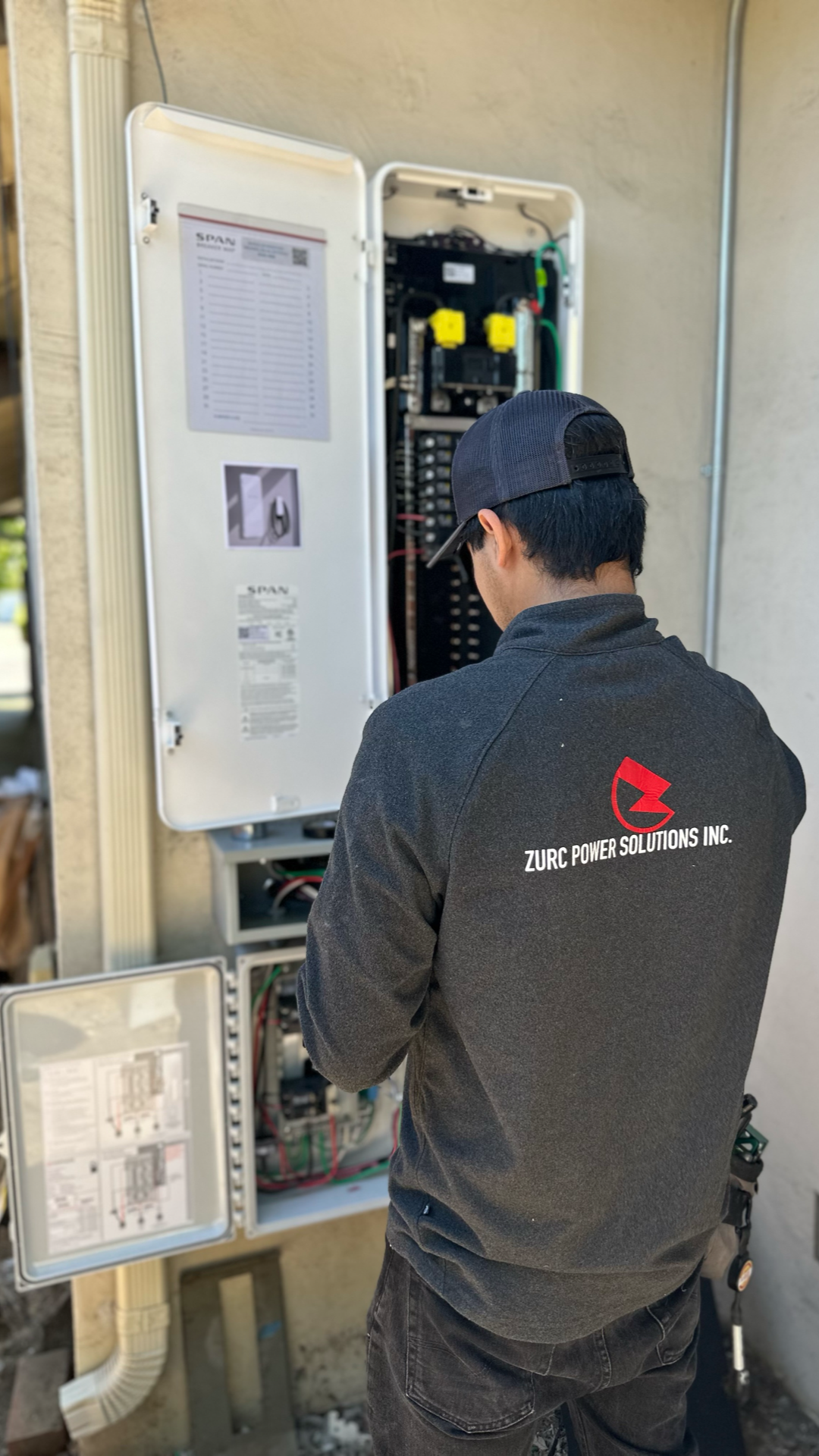 A man is working on an electrical box on the side of a building.