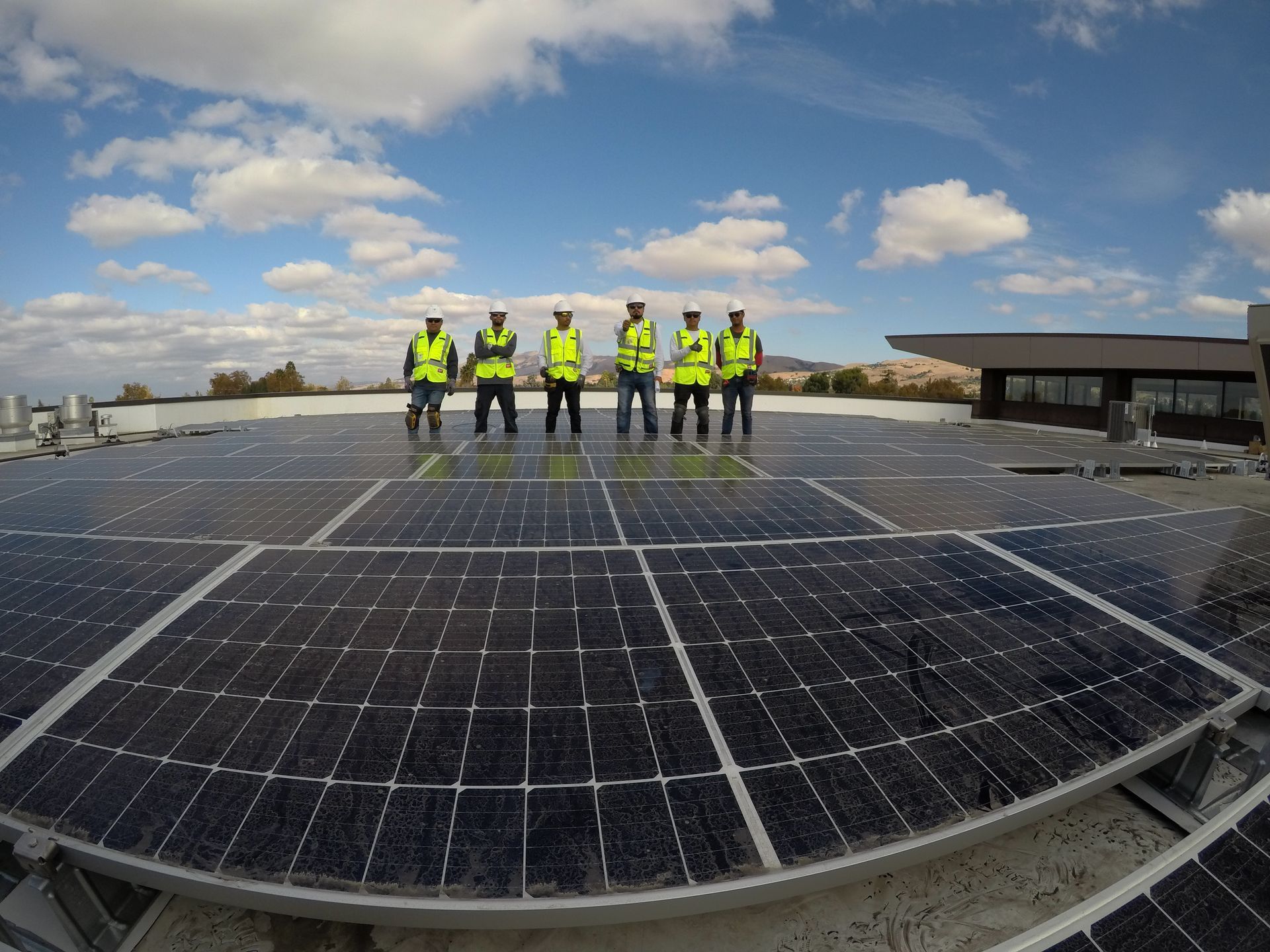 A group of men are standing on top of a roof with solar panels.