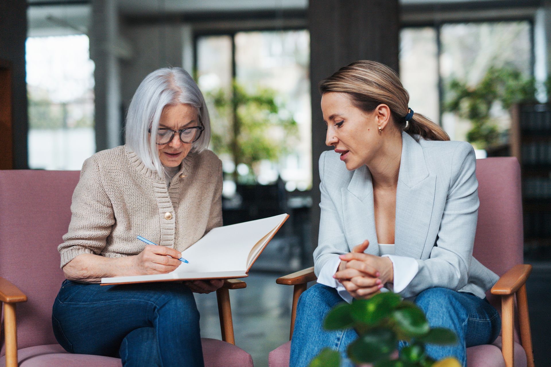 Two women are sitting on a couch looking at a clipboard.
