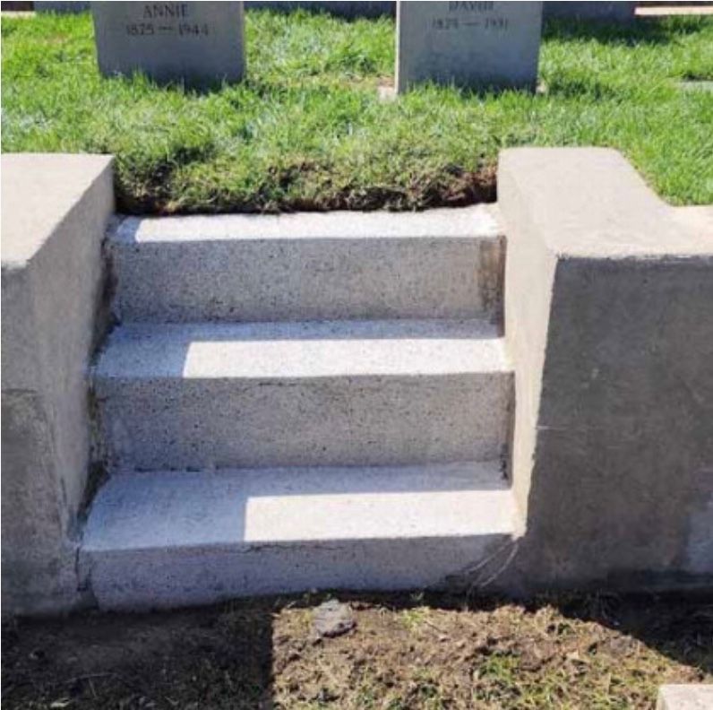 Three concrete steps lead up to a grass-covered area, flanked by concrete walls, at a cemetery.